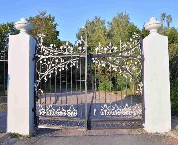 Large white metal driveway gate surrounded by trees and greenery