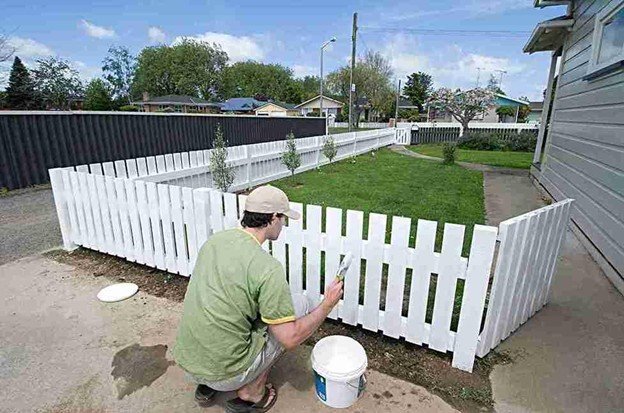 Contractor painting and finishing a newly installed cedar side-by-side fence along a residential yard for long-term protection.