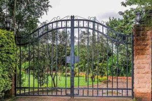 Black wrought iron double gate opening to a landscaped garden driveway